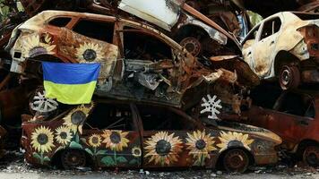 The national flag of Ukraine against the background of ruins and rusty metal of destroyed cars. A blue-yellow flag waving in the wind under the sun in a ruined city. Ukraine, Kyiv - April 29, 2023. video