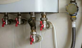 Hidden water taps for connecting a gas boiler on a tiled wall. Plumbing connections for a domestic double-circuit gas boiler. Pipes of the heating system. Installing a gas boiler with red taps. photo