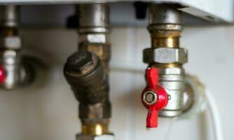 Hidden water taps for connecting a gas boiler on a tiled wall. Plumbing connections for a domestic double-circuit gas boiler. Pipes of the heating system. Installing a gas boiler with red taps. photo