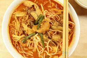 Malaysian curry yellow mee noodle with roasted chicken slice in white bowl chopstick on wooden background photo