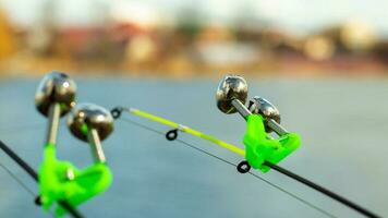 The bite alarm hangs on the tip of the fishing rod against the background of water. Fishing rod while fishing on the lake, river. Fishing tackle. Two rods with bite alarm. photo