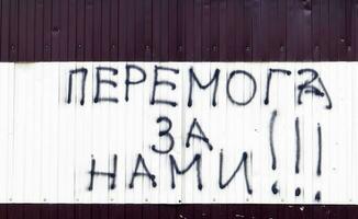The text on the wall is painted with black spray paint. Translation - victory is ours. Patriotic text in Ukrainian. The concept of peace, no war, victory in war. photo