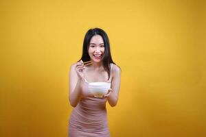 Beautiful young south east Asian woman holding chines empty chopstick Chinese soup spoon bowl utensil pretend acting posing see eat taste smell feed offer satisfaction yummy yellow orange background photo