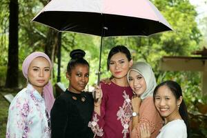 group of woman friends Malay Chinese Indian Asian outdoor park lake nature walking under one umbrella secure safe rain photo