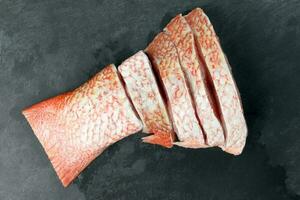 Cleaned descaled sliced red snapper fish fillet pieces black marble slate background photo