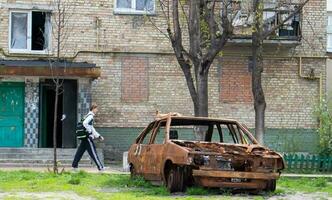 A broken car, shot by artillery, stands in the courtyard of a multi-storey residential building. War between Russia and Ukraine. The wreckage of an abandoned car. Ukraine, Kyiv - May 06, 2023. photo