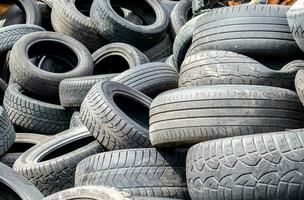 Garbage from a pile of black old car tires. Environmental pollution. Ecological problems. Old car tires thrown into an industrial landfill for recycling. Reuse of worn rubber tires. photo