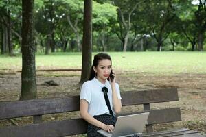 Young asian chinese woman outdoor on park bench use laptop computer think read look happy wonder serous front talk on phone photo