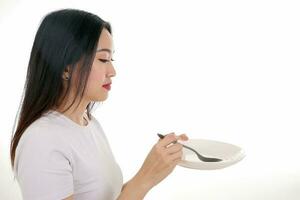 Beautiful young south east Asian woman pretend acting posing holding empty spoon in hand eat taste feed offer white background satisfaction yummy photo