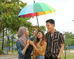 Young Asian Malay man woman outdoor green park walk talk discuss mingle under umbrella photo