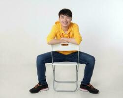 Young good looking Asian chinese malay man pose face body expression mode emotion on white background sit on reversed chair look photo