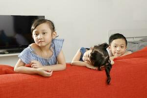 Three little child boy girl brother sister happy smile looking over the sofa photo