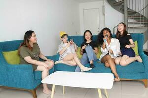 joven asiático mujer grupo hablar chisme charla canta fiesta divertido disfrutar emoción en azul vivo habitación sofá foto