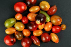 Fresh ripe mixed tomato verity assorted color on black background photo