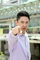 Young south east Asian man business office outdoor stand look at camera point finger angry photo