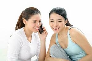 Two beautiful young south east Asian Chinese healthy workout sit on floor talk on phone ease drop gossip on white background photo