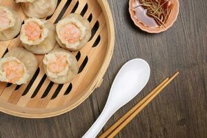 Prawn shrimp shaomai dim sum dumpling in bamboo steamer sauce chopsticks soup soon on rustic wood background photo
