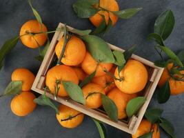mandarin orange green leaf in wooden box crate top view on black slate marble background photo