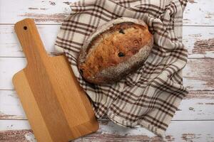 rústico todo grano artesano un pan pan con arándano pasa seco Fruta nueces envuelto en juego de damas paño con de madera el cortar tablero terminado mesa parte superior plano laico ver foto