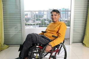 joven hombre sur este asiático malayo origen sentado en silla de ruedas en contra ventana ligero. paralizado cintura abajo debido a accidente foto