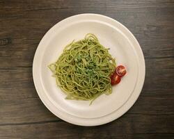 Asian style spaghetti with minced chicken spinach thai basil tomato garlic nutmeg olive oil presto sauce served on badge ceramic plate over on rustic wood background photo