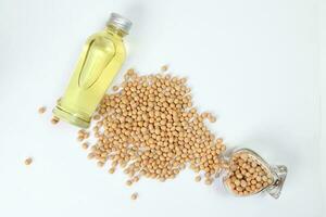 Soyabeans pouring from hart shape glass bottle around bottle of soya bean oil on white background photo