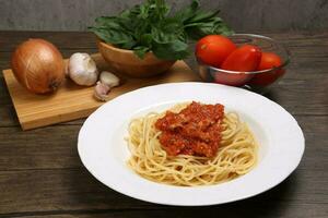Cooked spaghetti sauce on white plate with ingredients roma tomato glass bowl basil onion garlic wooden board recipe on table marble wall photo