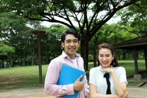 joven asiático malayo chino hombre mujer al aire libre parque caminar estar estudiar hablar discutir ordenador portátil archivo libro mochila actitud contento mezclarse Mira adelante foto