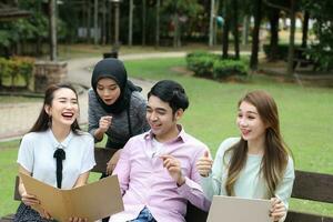 joven asiático malayo chino hombre mujer al aire libre parque libro archivo carpeta ordenador portátil computadora teléfono sentar estar estudiar mezclarse foto