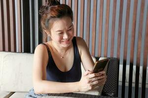 beautiful attractive middle age southeast asian woman resting sitting on sofa after exercise text looking smart phone dark wooden background waiting resting area photo