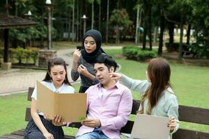 joven asiático malayo chino hombre mujer al aire libre parque libro archivo carpeta ordenador portátil computadora teléfono sentar estar estudiar mezclarse foto