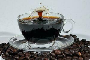 Coffee splash pillar in transparent glass cup saucer full of liquid coffee on coffee been bed white background photo