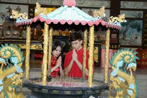 Young south east asian Chinese man woman traditional costume cheongsam praying outdoors at temple photo