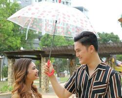 Young Asian Malay man woman couple outdoor green park walk talk discuss mingle under umbrella photo