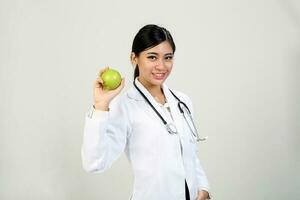 joven asiático hembra médico vistiendo delantal uniforme estetoscopio participación sano verde manzana foto