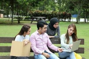 Young asian malay chinese man woman outdoor on park bench study talk discuss point laptop file book photo