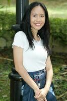 One Asian Chinese  woman posing smile look forward towards camera confident outdoor green park photo