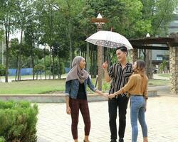 Young Asian Malay man woman outdoor green park walk talk discuss mingle under umbrella photo