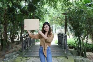 Young Asian Malay woman outdoor green on wooden bridge pose hold board copy text space photo