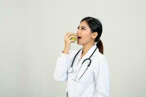 Young Asian female doctor wearing apron uniform stethoscope holding eating healthy green apple photo