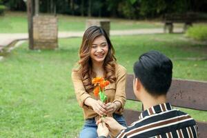 Young Asian Malay man woman couple outdoor green park sit on bench kneel propose love photo