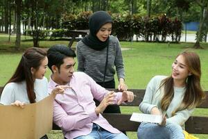 Young asian malay chinese man woman outdoor on park bench study talk discuss point laptop file book photo