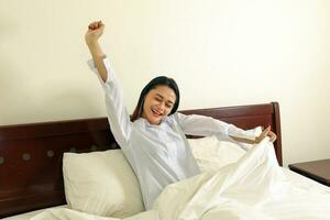 joven hermosa moderno malayo mujer relajarse Mañana despertar arriba en cama sonrisa brazos en aire tramo foto