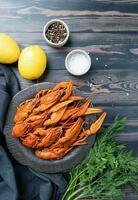 cooked crawfish on black plate with lemons and spices on wooden background photo