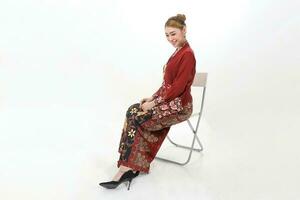 Asian woman traditional red maroon kebaya sharong on white background sitting pose chair sit photo