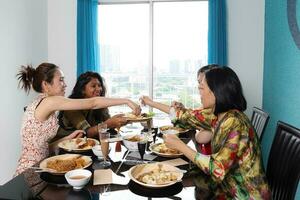 Young southeast asian woman group talk celebrate eating enjoying food rice curry noodle chicken drink cheers on dining table photo