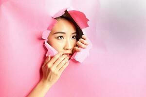 joven hermosa asiático mujer expresión mediante Rasgado papel agujero foto