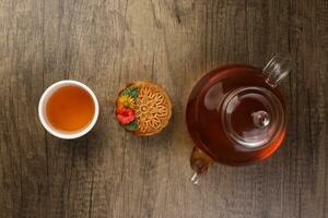 Colorful flower decorated mooncake cut slice half layer Chinese mid autumn festival on glass teapot white ceramic teacup over rustic wood border photo