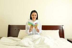 Young beautiful modern Malay woman read book lying sitting on bedroom bed photo