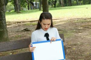 joven asiático chino mujer al aire libre parque instalaciones libro archivo carpeta ordenador portátil computadora teléfono sentar estar estudiar mezclarse foto